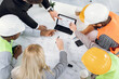 © sofiko14 - Top cropped shot of multiethnic men and woman sitting together at table and discussing blueprints during business conference. Multi ethnic architects, designers and engineers working at office.