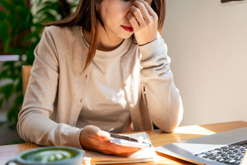 Wall Mural - Tired and stressed young Asian woman sitting at her working place with a cup of coffee and breakfast in the morning