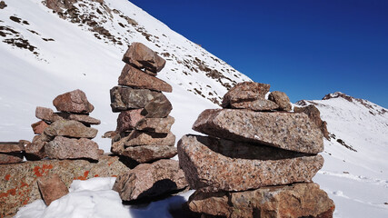 Stone pyramid pointer tour in the snowy mountains. Stone pyramids serve as pointers to the route. All around is snow, peaks, blue sky and rocks. Climbing in the mountains. Almaty, Kazakhstan.