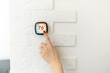 © Angelov - Smart home digital thermostat touch screen woman touching touchscreen to adjust temperature of heating in living room wall