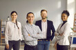 © Studio Romantic - Portrait of successful young asian male executive in office against colleagues background. Smiling confident man with folded arms posing looking at camera. Confidence and business concept.