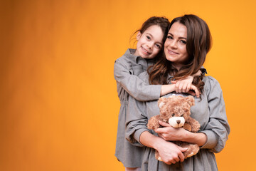 Wall Mural - Mom holding a toy bear and daughter in pigtails hug and look at the camera. Family holiday