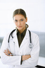 Wall Mural - Woman-doctor standing with arms crossed and looking at camera. Perfect medical service in clinic. Medicine and healthcare