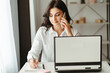 © Vadym - Young business woman multitasking working with laptop and documents and speaking by phone. Productivity. Cozy office workplace, people at work, e-learning concept
