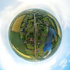 little planet pano - summer landscape over a farm near a blue lake under the sky with storm clouds a