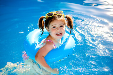 little girl with glasses in the swimming pool in the swimming circle, children's summer vacation on the weekend