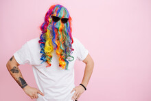 A Man Jokingly Put On A Multi-colored Wig And Glasses On His Head, Posing Against A Pink Studio Background.