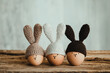 Three Easter eggs in crochet hats with bunny ears on old wooden table