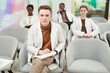 © Seventyfour - Front view portrait of young man looking at camera while sitting in audience and listening to lecture on medicine in college or coworking center, copy space