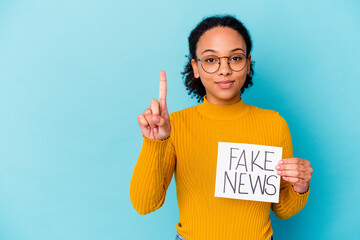 Young african american mixed race woman holding a fake news concept showing number one with finger.