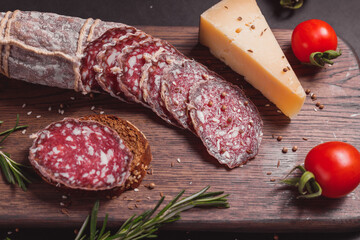 Smoked ham sausage and cutted slices with rosemary and cherry tomatoes on dark wooden board