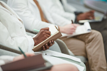 Multi ethnic group of young people wearing lab coats while sitting in row in audience and taking notes in lecture on medicine, copy space