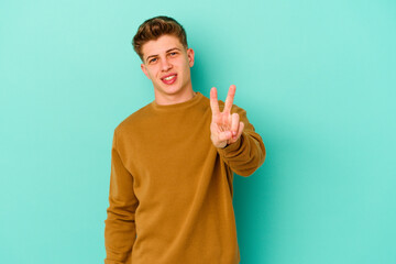 Young caucasian man isolated on blue background showing victory sign and smiling broadly.