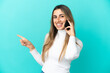 © luismolinero - Young caucasian woman using mobile phone isolated on blue background pointing finger to the side