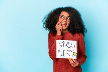 Young african american curly woman holding a virus alert placard relaxed thinking about something looking at a copy space.