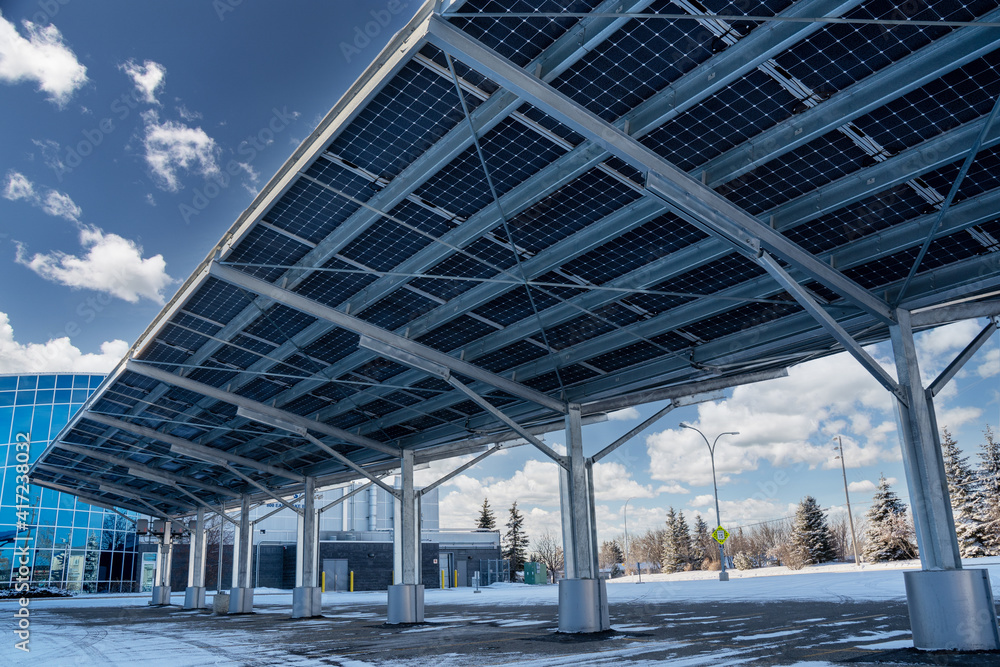 A modern solar carport for public vehicle parking is outfitted with solar panels producing renewable energy. - obrazy, fototapety, plakaty 