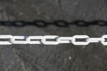Close-up View Of A Segment Of A Heavy White Plastic Chain Closing Off A Driveway And Its Shadow On The Ground