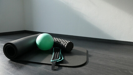 Wall Mural - green ball fascias roll and weight bands on a gym mat on dark background - gym equipment in sunbeam - copy space