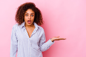 Wall Mural - Young african american woman isolated on pink background impressed holding copy space on palm.