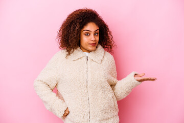 Wall Mural - Young african american woman isolated on pink background doubting and shrugging shoulders in questioning gesture.