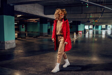 Young Smiling Fashionable Woman With Curly Hair Walking In Underground Garage And Looking Away.