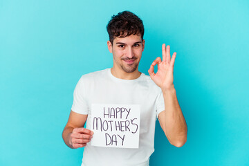 Wall Mural - Young caucasian man holding a happy mothers day placard isolated cheerful and confident showing ok gesture.