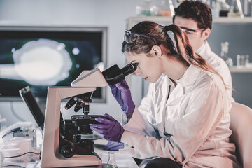 Poster - Life scientists researching in laboratory. Attractive female young scientist and her doctoral supervisor microscoping in their working environment. Healthcare and biotechnology.