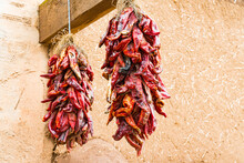 Two Bunches Of Dried Hot Red Chili Peppers Hanging Outside Of An Adobe Building In New Mexico