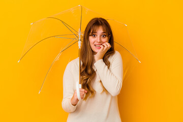 Wall Mural - Young caucasian woman holding a umbrella isolated biting fingernails, nervous and very anxious.