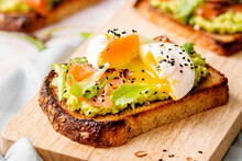 Smoked Salmon Toast With Avocado Cream And Open Poached Egg On Top, With Creamy Yolk Dripping.