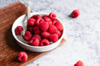 © The Picture Pantry - Fresh raspberries in a shallow dish with a spoon sitting on a cutting board.