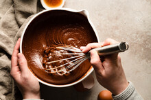 Hands Mixing A Bowl Of Brownie Batter Next To Bowls Of Flour And Chocolate Chips.