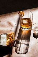 Whiskey In Hard Light With Orange Spirals Next To A Small Bowl With Ice Cubes.