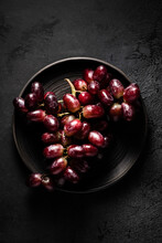 A Bunch Of Red Grapes Sitting On A Dark Plate In Moody Lighting.