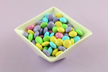 Sticker - Pastel Easter candy coated milk chocolate candy pieces in white candy dish on lavender background