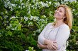 © Elena  - Portrait of a fat plump young blonde woman blooming with an apple tree on a white floral background in a park on a spring day. Happy plus-size girl with her eyes closed enjoying spring.