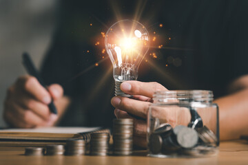 Poster - businessman holding lightbulb with using calculator to calculate and money stack. idea saving energy and accounting finance in home office concept, Business, finance, investment, Financial planning.