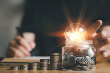 Poster - businessman holding lightbulb with using calculator to calculate and money stack. idea saving energy and accounting finance in home office concept, Business, finance, investment, Financial planning.
