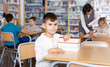 © JackF - Portrait of tired preteen boy sitting at desk with pile of books in classroom..