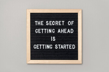 Wall Mural - The secret of getting ahead is getting started. Motivational quote on black letter board on gray background. Concept inspirational quote of the day. Greeting card, postcard