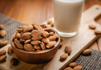 Wall Mural - Almond milk in the glass with almond in the wooden bowl on the wooden table.