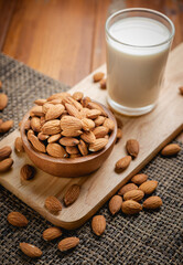 Wall Mural - Almond milk in the glass with almond in the wooden bowl on the wooden table.