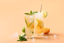 Two summer cold lemonade or mojito cocktail with orange and lime slice on color beige background. Refreshing beverage.