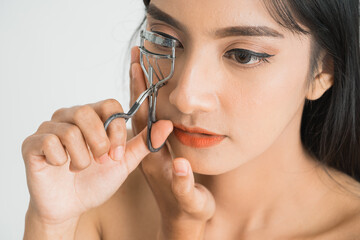 Beautiful young asian woman with eyelash curler on white background