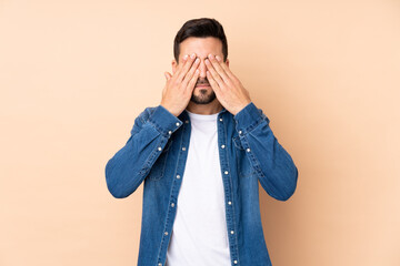 Poster - Caucasian handsome man isolated on beige background covering eyes by hands