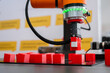 © zyabich - Pick and place robotic clamp arm manipulator moving red toy blocks at modern robot exhibition, trade show - close up view. Manufacturing, industrial, engineering, ai, automated technology concept