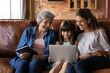 © fizkes - Happy three generations of Latino women sit relax on couch at home using modern electronic gadgets together. Smiling little Hispanic girl with mom and grandmother rest indoors have fun with devices.