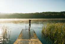 Woman Standing On Jetty And Looking At Lake