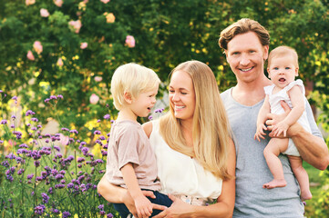 Happy young family with baby girl and toddler boy enjoying nice day in summer garden