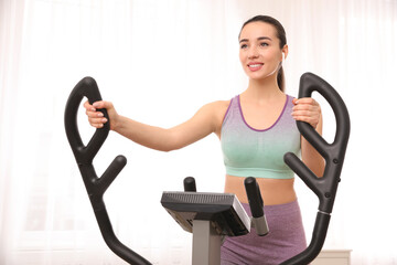 Canvas Print - Young woman using modern elliptical machine indoors